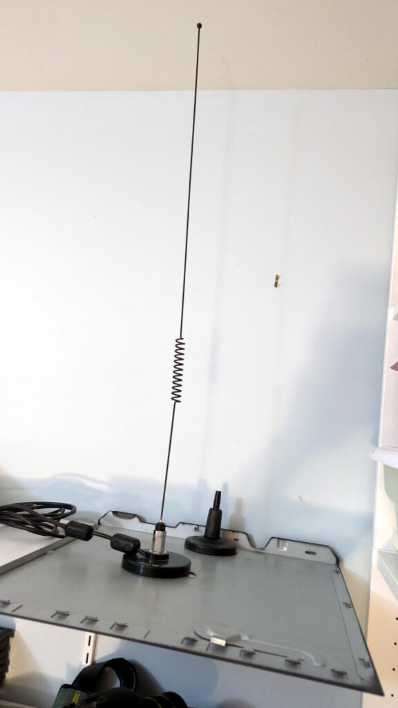 A dual band (2m/70cm) mag mount antenna on a metal sheet sitting on a shelf